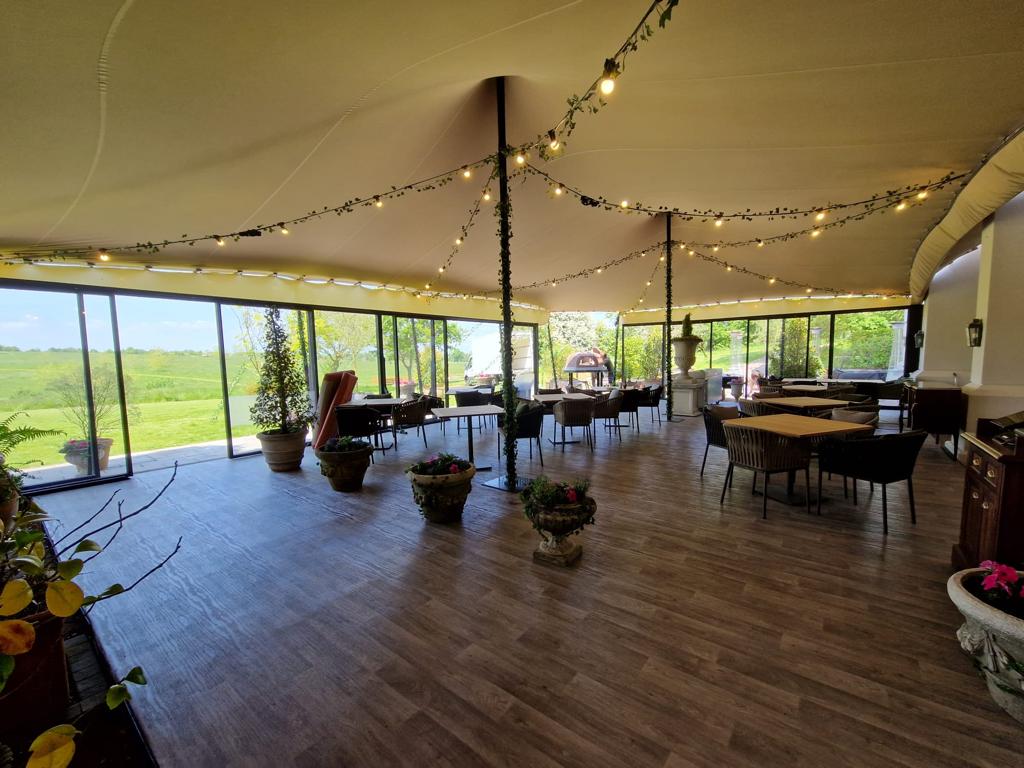 Clear-walled stretch tent set for dinner with festoon lighting overhead