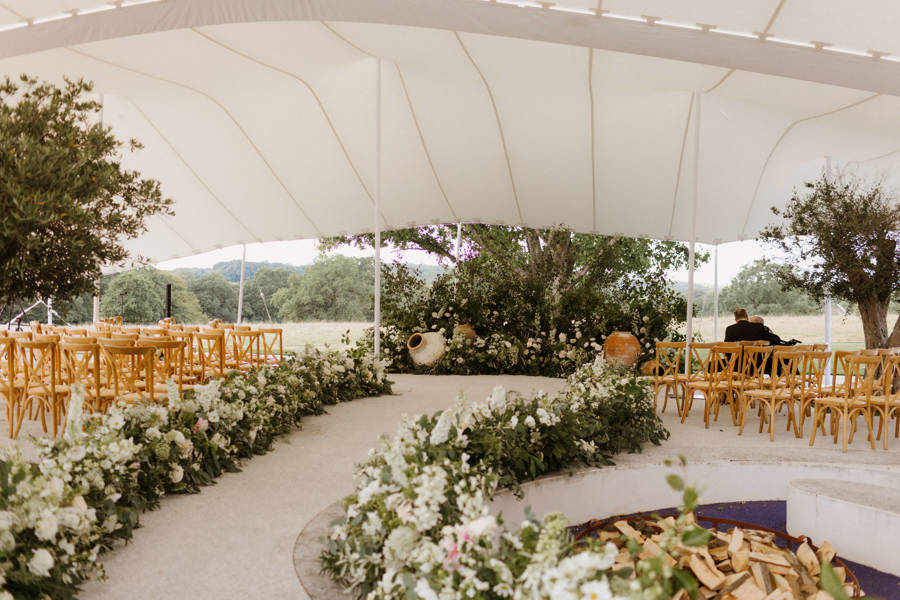 Wedding ceremony aisle and timber chairs beneath a white stretch tent