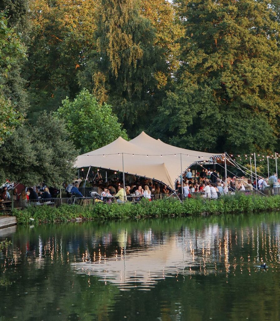 Lakeside festival bar under a cream stretch tent with festoon lighting