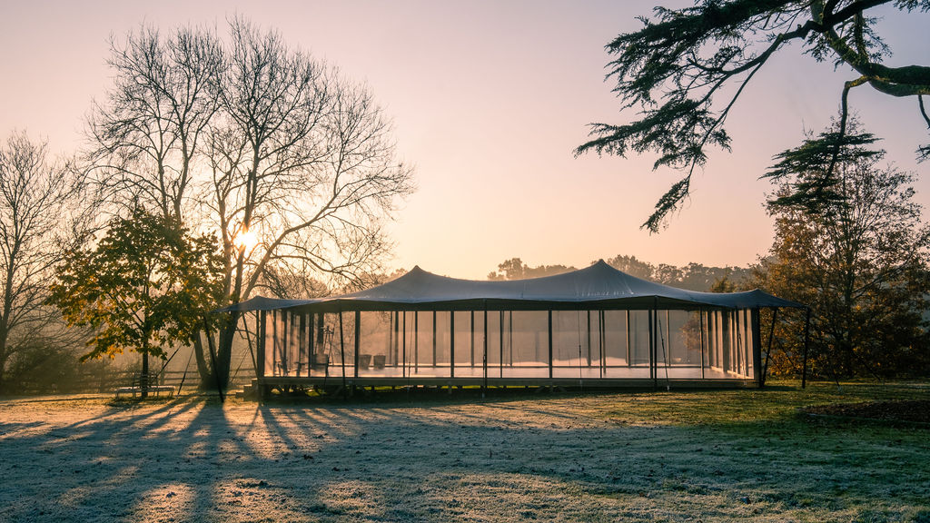 Glass-walled stretch pavilion on a frosted lawn at sunrise