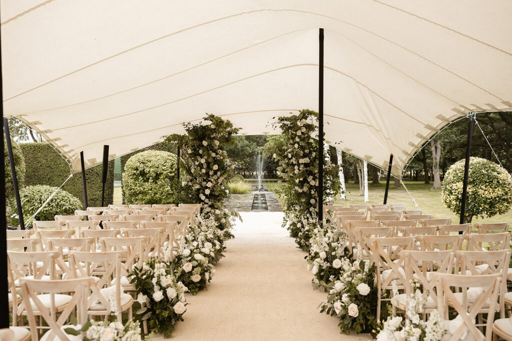 A wedding ceremony under a cream stretch canopy in a formal topiary garden