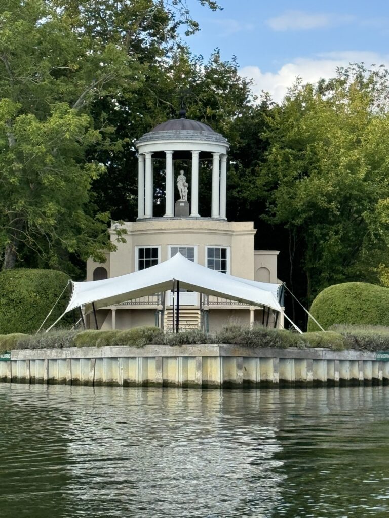 Small peaked stretch tent in landscaped grounds beside water