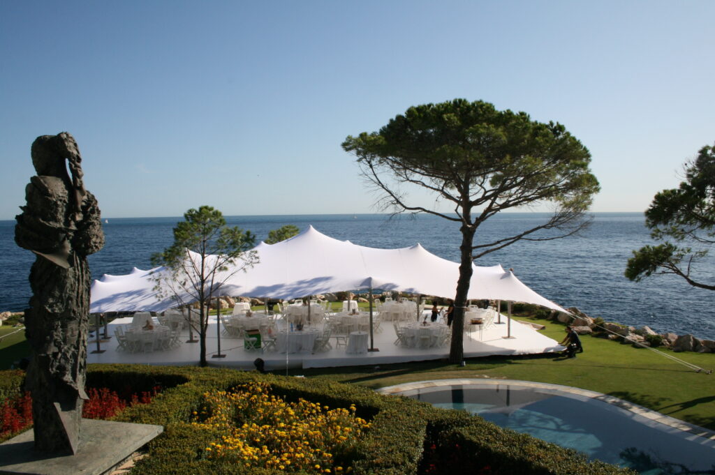 Coastal wedding reception with round tables under a peaked stretch tent