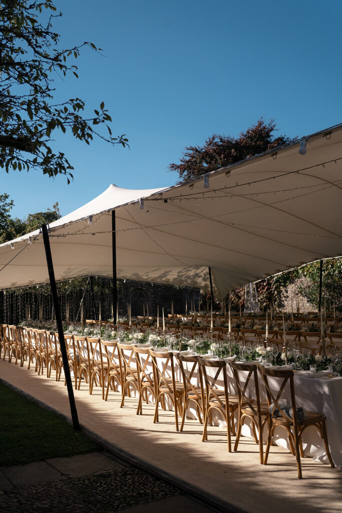 Wedding banquet tables and florals under an open-sided white stretch tent