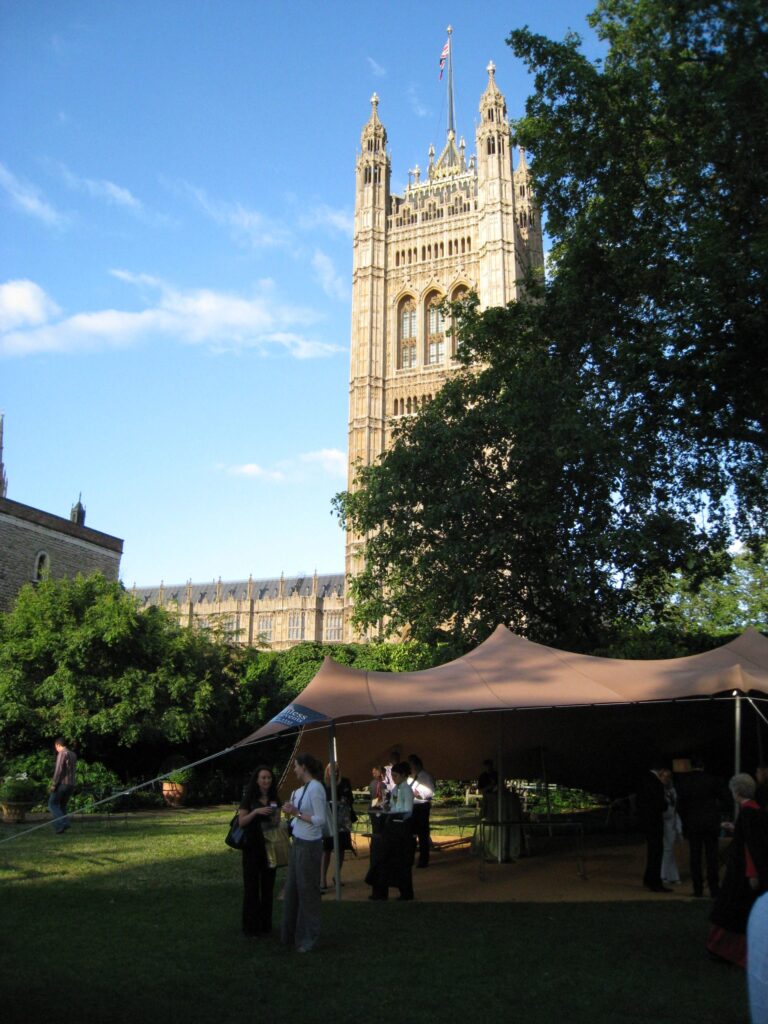 Cocktail tables under a tan stretch tent in a garden setting